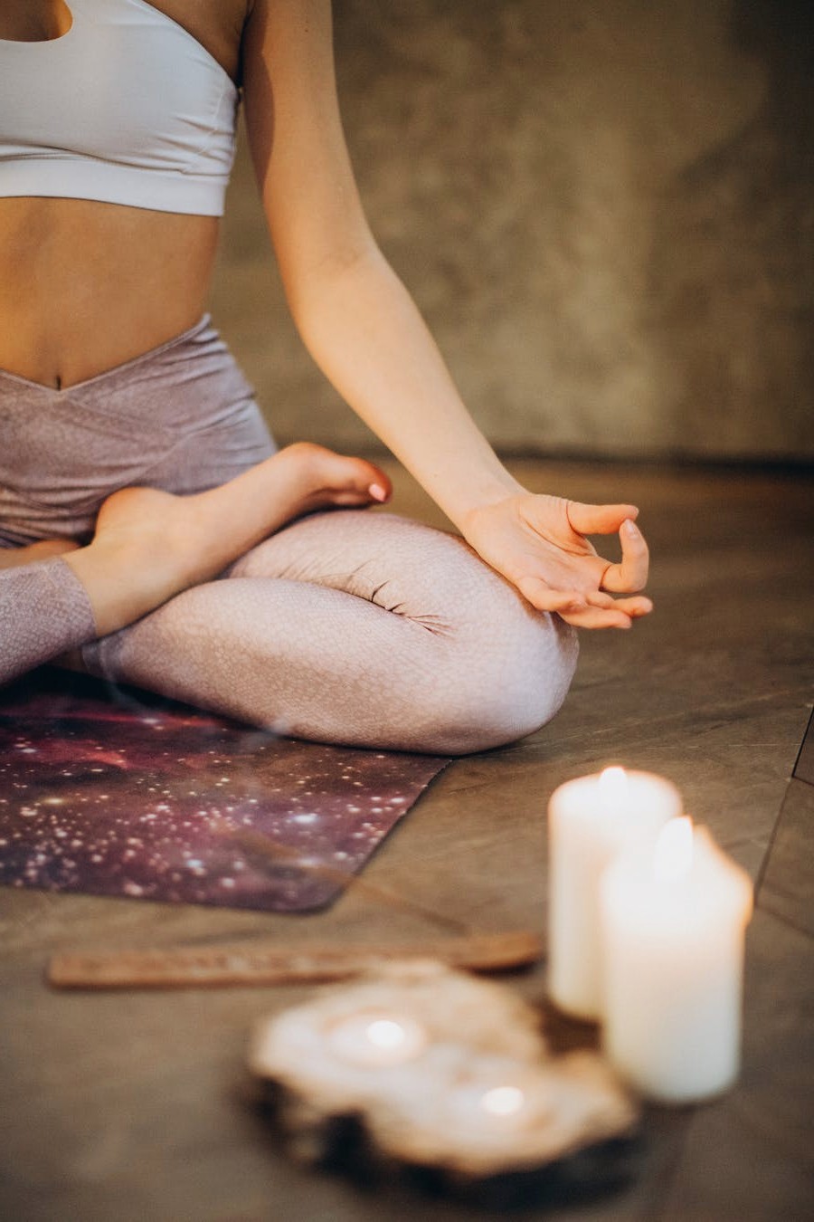 Person in cross-legged meditation pose on a yoga mat indoors beside lit candles